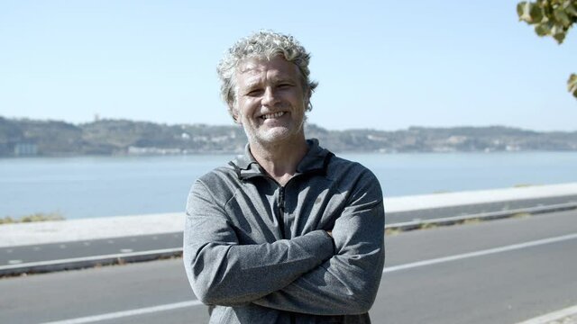 Positive Active Older 60s Man In Sportswear Standing With Arms Crossed, Looking At Camera And Smiling After Outdoor Morning Workout. Medium Shot. Elderly Age And Lifestyle Concept