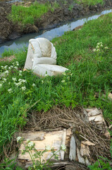 Illegal pile of old garbage and a discarded armchair on the background of nature
