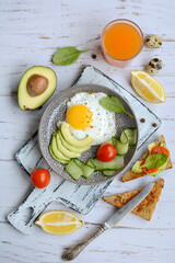 Vertical composition of a plate with scrambled eggs, toast with avocado and tomatoes, juice and lemon slices on a cutting board on a light background. Vertical