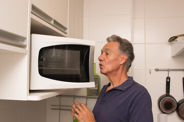 Senior man in his kitchen looking into his microwave oven