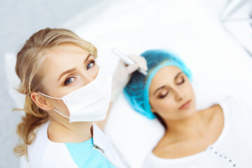 Naklejka premium Professional beautician doing eyebrow tattoo at woman face. Permanent brow makeup in beauty salon, closeup. Cosmetology treatment