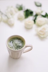A cup of green tea with white roses on white background view from above. Flatlay, top view, copy space