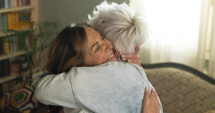 Cinematic shot of  happy senior grandmother and granddaughter are having fun together and hugging with affection in living room at home. Concept: life, grandparents, generation, love, care, family