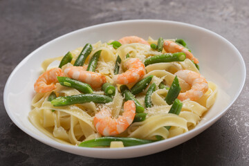 A view of a plate of Tagliatelle pasta with shrimps and green beans with grated Parmesan cheese on dark table. Italian food. Mediterranean cuisine.