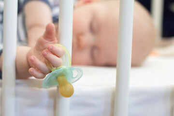 Little baby boy peacefully sleeping in the bed holding pacifier dummy in his hand