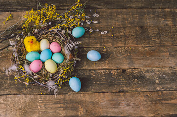 Yellow cute chicken with Easter eggs in the nest. Against the background of a wooden board.