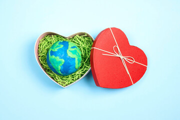 Planet in a heart gift box on a blue background. Earth Day concept.