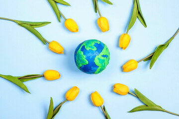 Planet Earth surrounded by yellow tulips  on a blue background. Earth Day concept.