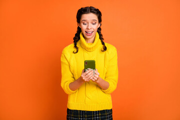 Portrait of cheerful pretty girl look phone unexpected follow comment isolated on orange color background