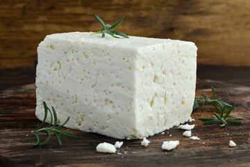 Fresh homemade cheese with rosemary sprigs on an old wooden board close-up.