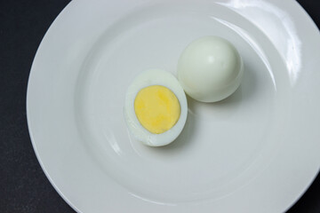 A boiled egg cut in half on a plate. Healthy breakfast. Boiled egg on black background