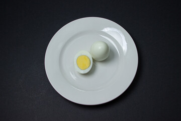 A boiled egg cut in half on a plate. Healthy breakfast. Boiled egg on black background