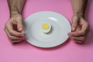 A boiled egg cut in half on a plate. Hands at breakfast. Healthy breakfast. Boiled egg on a pink background.