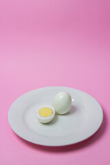 A boiled egg cut in half on a plate. Healthy breakfast. Boiled egg on pink background