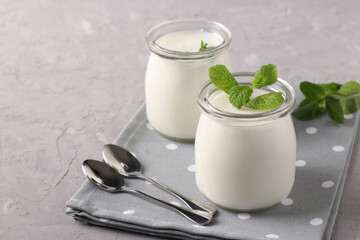 Homemade natural organic yogurt and mint in two glass jars on a grey background. Closeup
