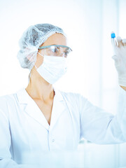 Fototapeta premium Professional female scientist in protective eyeglasses researching tube with reagents in laboratory toned in blue. Concepts of medicine and science researching