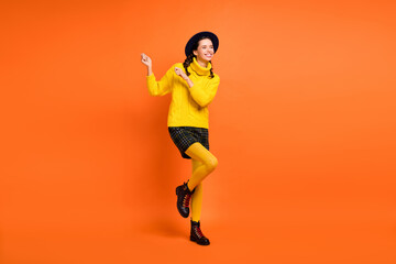 Fototapeta na wymiar Full size photo of optimistic cute girl dance wear yellow sweater cap skirt shoes isolated on orange background