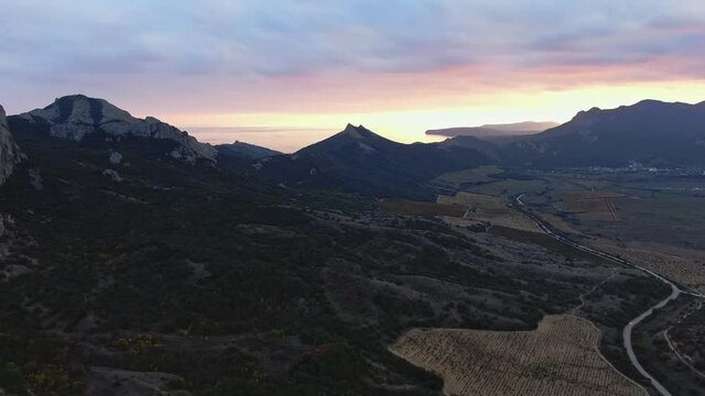 Bright glow of sunset under a cloudy sky over a mountain range and vineyards in a valley