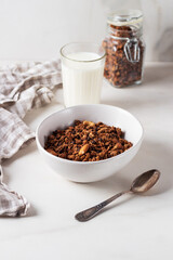 Homemade chocolate granola in a white plate with milk on a light background. Healthy breakfast
