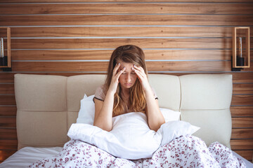 Unhappy girl in a bedroom. Sleepy young woman feeling drowsy or dizzy after waking up in bed, suffering from lack of sleep deprivation, insomnia, morning headache or migraine, having hangover 