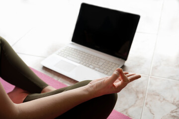 Woman yoga meditation in lotus position, watching online fitness class in computer.Virtual yoga tutorial,video call concept.Laptop with blank black screen mockup for promo or text with copy space.