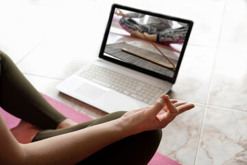 Online yoga sport fitness training concept.Woman in lotus position watching in computer online class, tutorial or video call.Meditation and relax healthy training exercises.