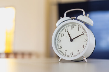 white alarm clock analog with bell on table in the morning inside house. equipment hurry wake up sleepy.