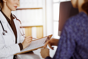 Doctor and patient discussing current health examination while sitting in sunny clinic. Perfect...