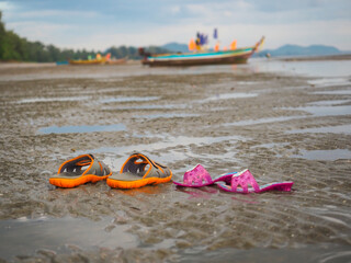 Colourful two couple of slippers put on the sandy beach and fishing boat onbackground