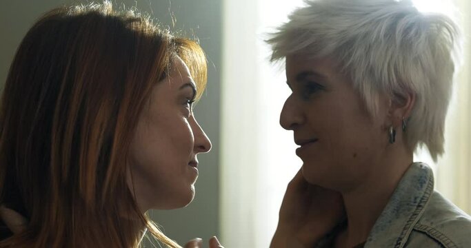 Cinematic close up of carefree happy homosexual female gay and transgender man couple in love is enjoying time together is hugging and kissing with affection as sign of timeless forever love at home.