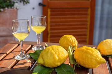 Lemons with leaves, lemonade or limoncello in a glass glass, on a wooden table on the terrace.