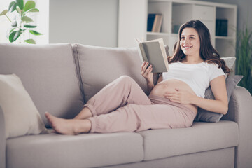Full size photo of attractive young woman mom hold read book lie couch touch belly indoors inside house