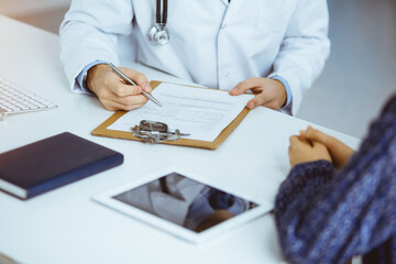 Unknown bearded doctor and patient woman discussing current health examination while sitting in sunny clinic, close-up