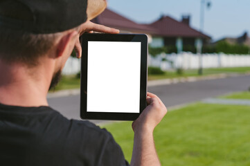 A tablet in the hands of a man, against the backdrop of a house.