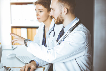 Red-bearded doctor with female colleague discussing current disease therapy while sitting at...