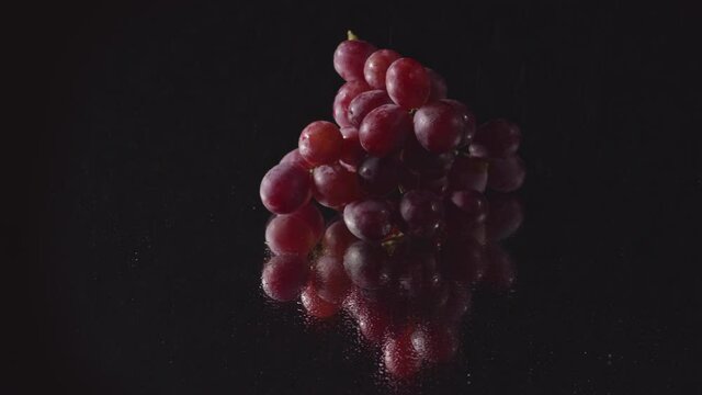 .A bunch of grapes Placed on a mirror with water droplets with a black background are turning.