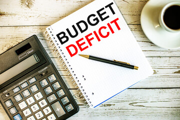 BUDGET DEFICIT written on white paper near coffee and calculator on a light wooden table. Business concept