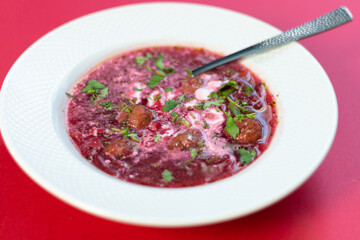 beetroot soup borscht with meatballs, sour cream, cilantro, spoon in white bowl on red background