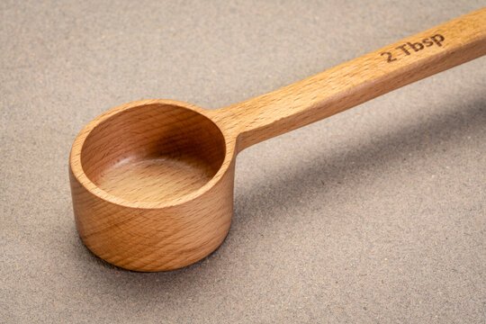 empty wooden measuring scoop (2 tablespoons) against textured paper background