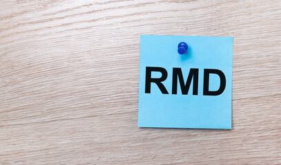 On a light wooden background - a light blue square sticker with the text RMD Required Minimum...