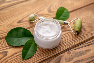 Jar of cream, green leaves and facial massager. Concept of skin care and use of cosmetics with a natural organic composition