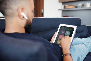 Close-up image of man using home control application on digital tablet when resting on sofa