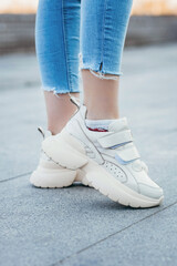 Fototapeta na wymiar White sneakers on girl legs on the street background