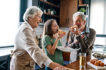 Grandparents and child together in kitchen eating pizza