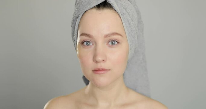 Beautiful young european woman doing patches under her eyes after a shower before going out on a gray background. Concept of personal care and beauty treatments