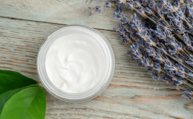A jar of cream, green leaves and lavender on a wooden table. Top view. Concept of skin care and choice of cosmetics with a natural organic composition