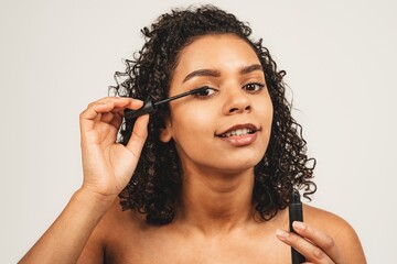 Close up photo of face natural beauty attractive black woman using mascara. Isolated over white background. Natural beauty and health