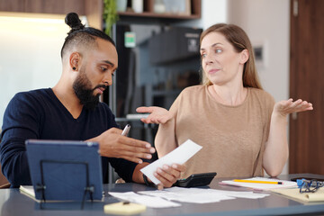 Serious man showing unpaid bill to confused wife when they are dicussing family budget