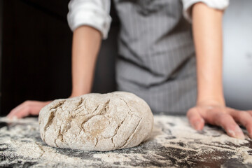 Prepared dough lies on the table sprinkled with flour, against the background of the baker hands. Bread making. 