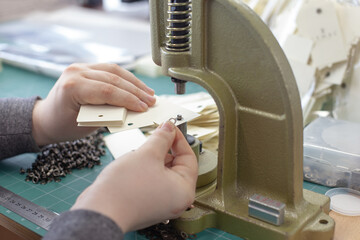 close-up hands man put grommets and eyelet in a stack of blanks clothing tags on a large manual...